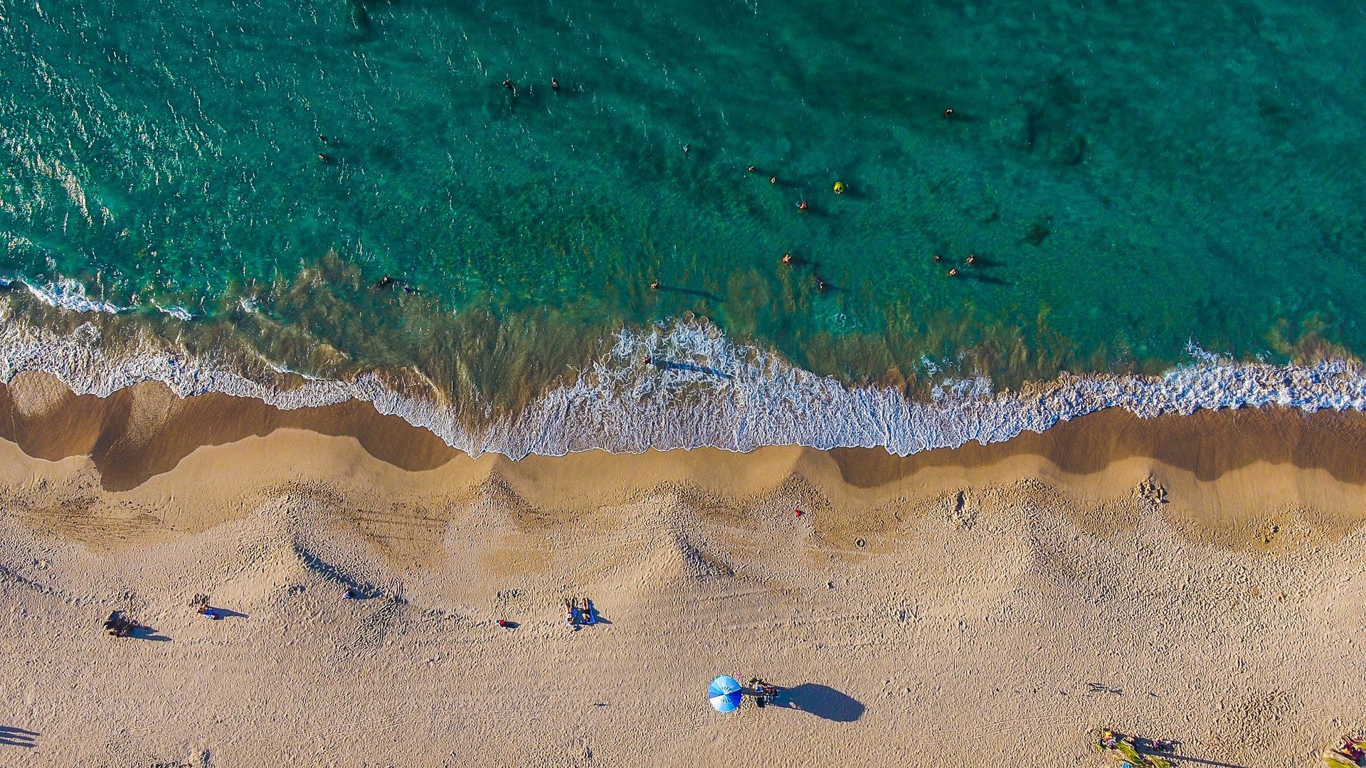 aerial view of blue-green waters and a sandy beach with people appearing in distance