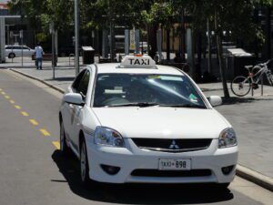 taxi in Adelaide represented in a white vehicle with a taxi signage on top, driving on the road