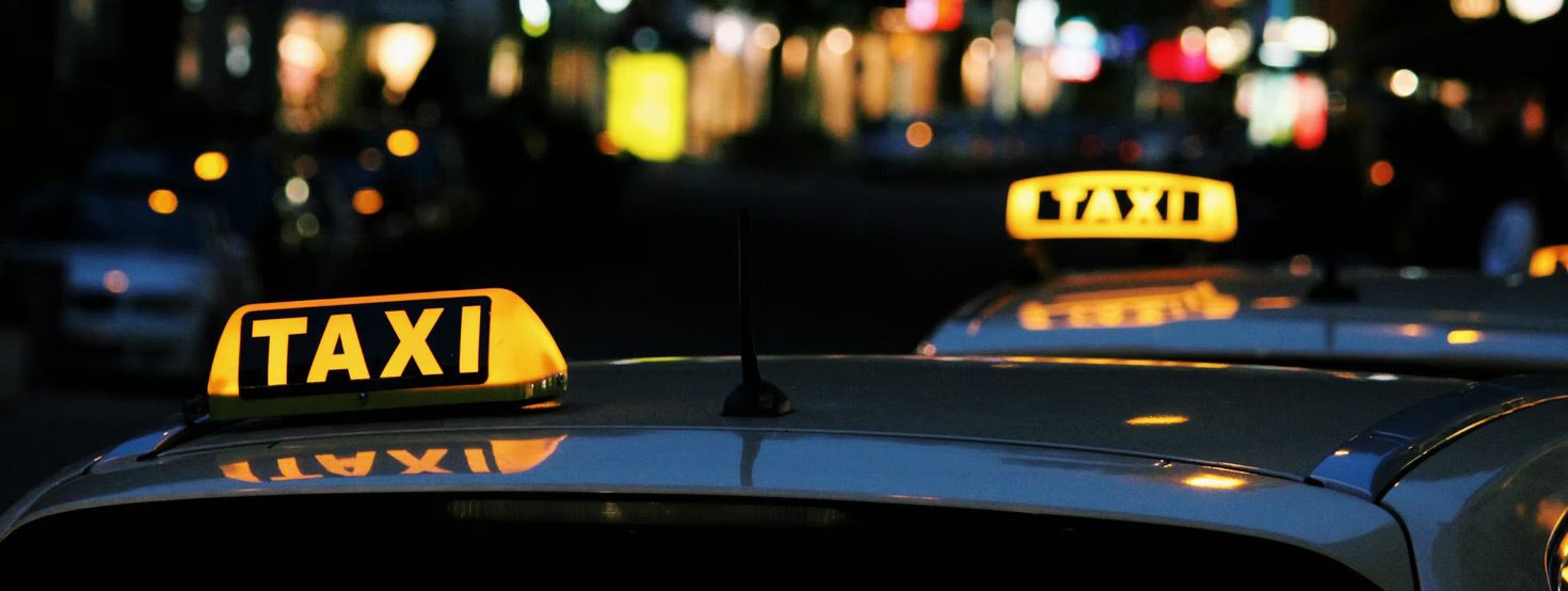 Houston taxi yellow and black lighted taxi signs being reflected on top of two dark coloured taxi at night time