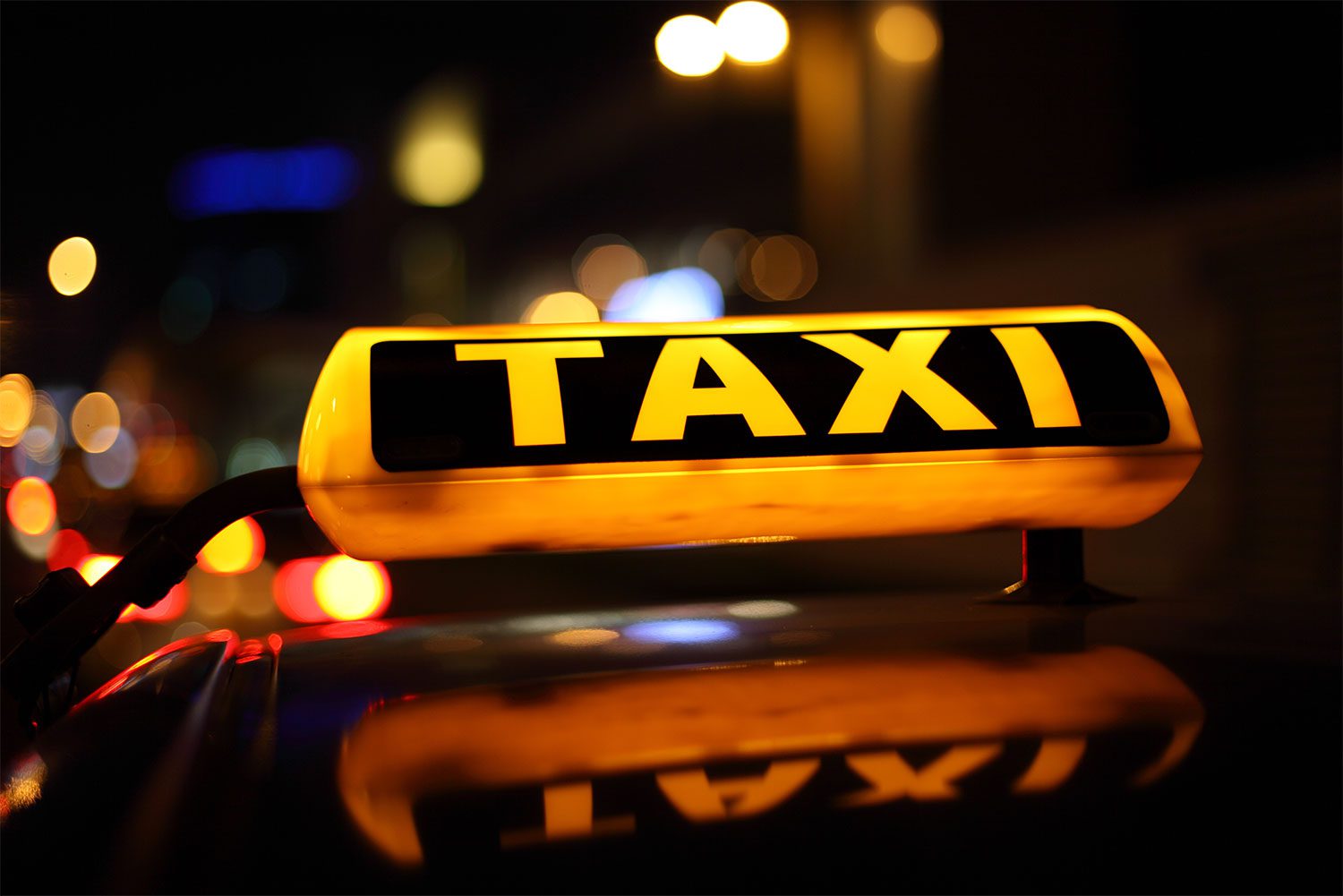 New Orleans taxi yellow and black lighted taxi signage being reflected on top of a dark coloured taxi at night time