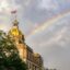 shot of the city hall's top, half covered by a green tree under a cloudy sky, right after thunderstorm, with a vivid rainbow showing