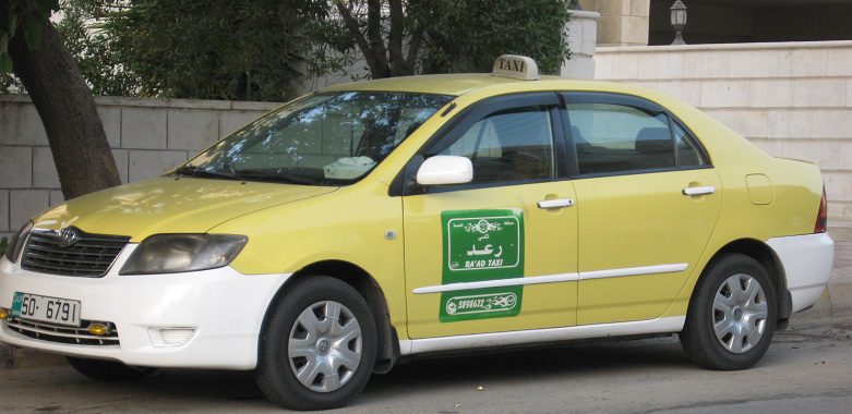 Amman taxi yellow taxi with white bottom part with white sign on its roof and black letters