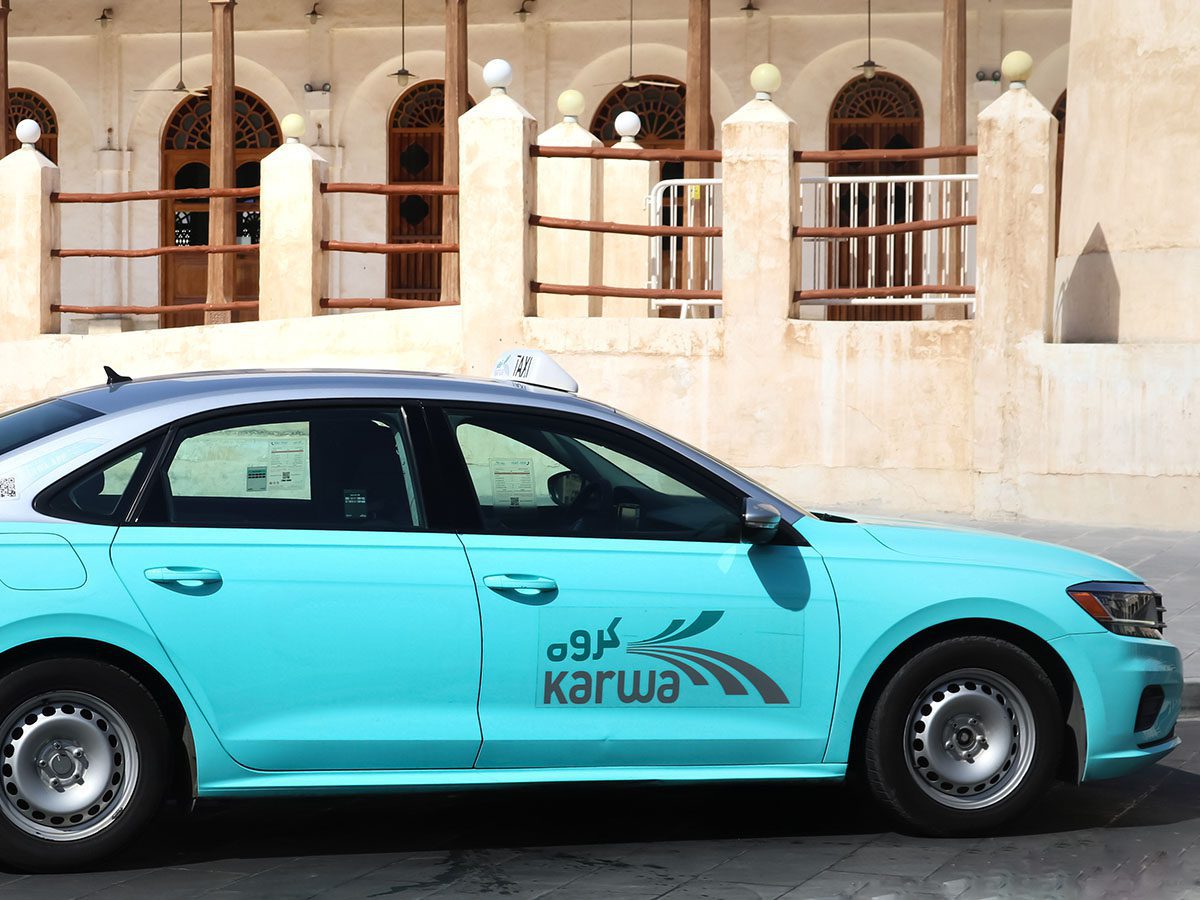 A,View,Of,Taxi,Service,In,Doha,,Qatar,-,05th neon blue coloured taxi with white and black taxi sign on the roof in front of concrete building