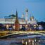 lights across bridge in Moscow reflecting onto the river underneath with city buildings in distance as it gets to nighttime