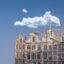 low angle photography of concrete building topped with a statue under a blue sky and sparse white fluffy clouds