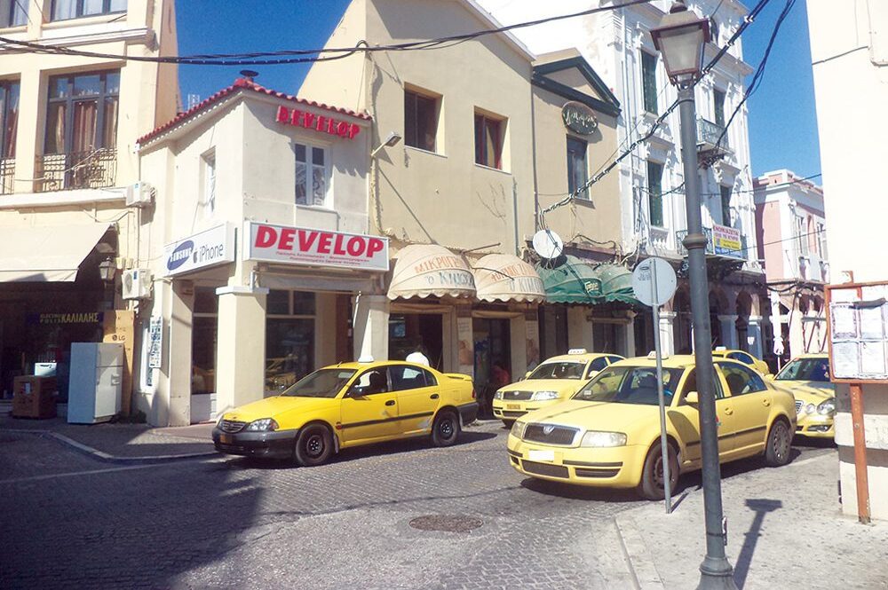 Mytilene taxi yellow cabs parked in the street with pale yellow houses in the background