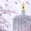 Gold statue on top of concrete grey building with pink cherry blossom trees nearby