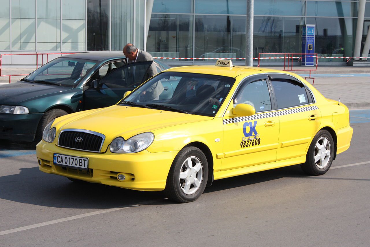 sofia taxi bulgaria yellow taxi with company sign on the front door passing another car in front of the airport