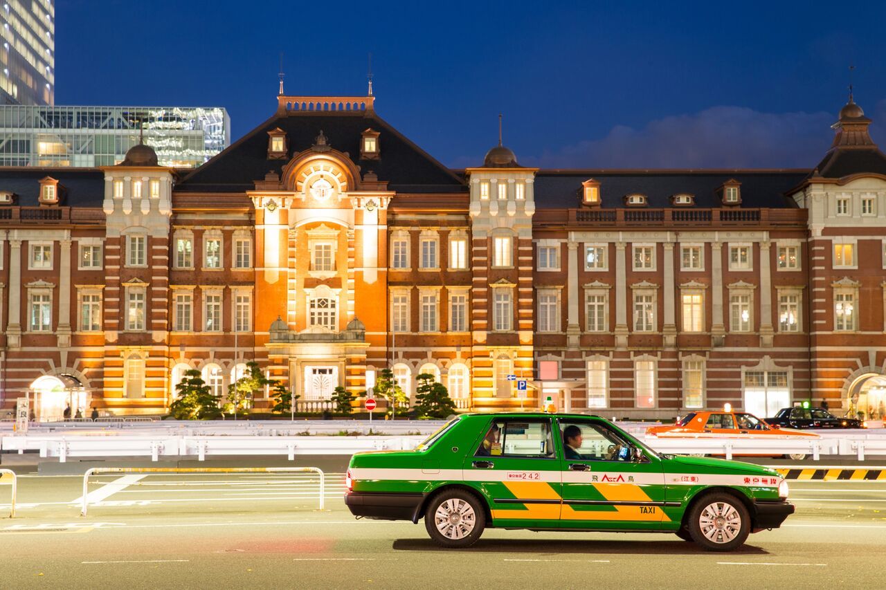 Tokyo taxi green taxi with yellow details driving in the street with a lighted buidling in the bakground