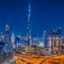 Night view of downtown Dubai with the Burj Khalifa lit up among modern skyscrapers and busy highways, showing the vibrant city travelers reach easily by airport taxi in Dubai.
