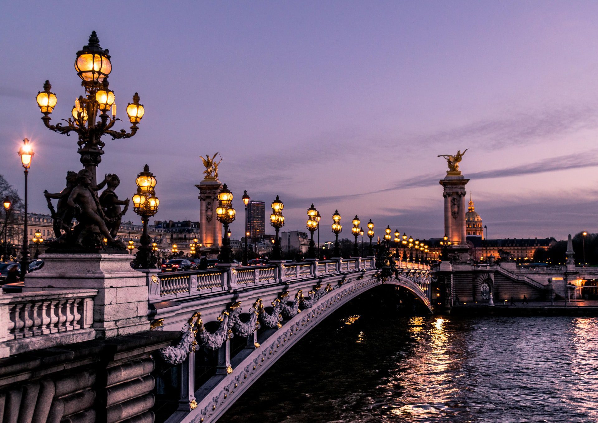Parisian bridge with lights over a body of water at dusk.