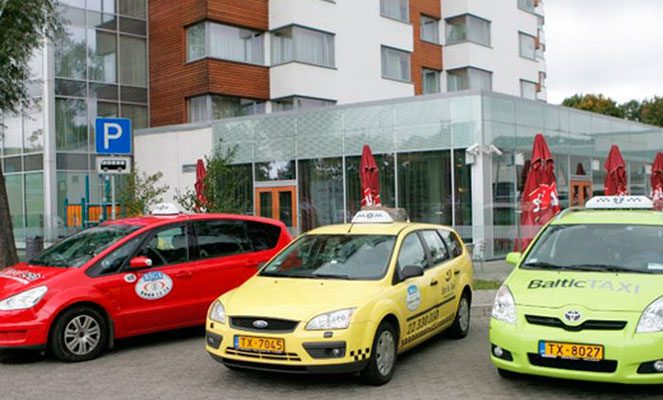Riga taxi a red, a yellow and a neon green taxi parked next to each other, all with signature white taxi signage on their roof