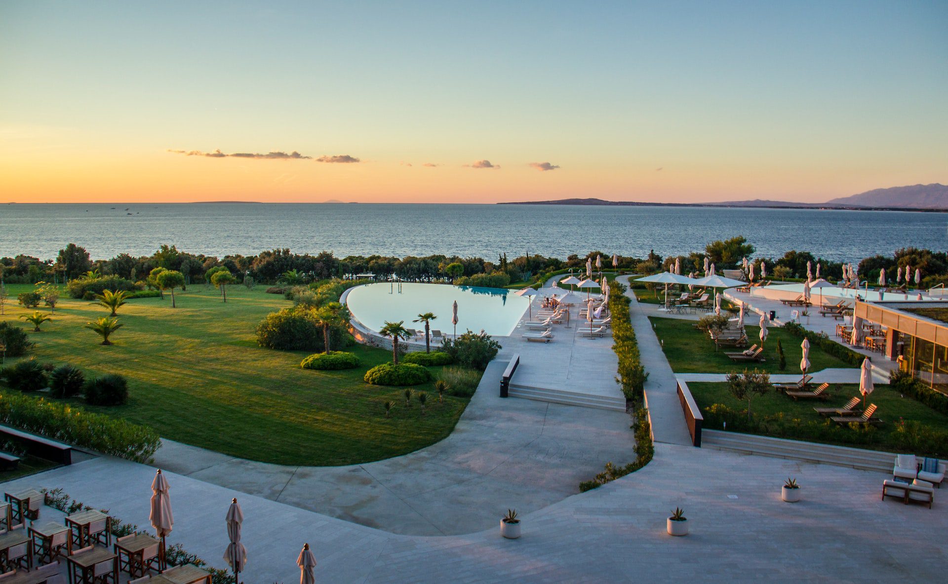 sun rising in Zadar, summer resort with green grass and trees, swimming pool and sun loungers by body of water