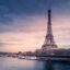 Eiffel Tower in distance by body of water with boats under a cloudy sky