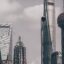 grey cloudy sky appearing behind 5 dominant modern city buildings with birds travelling west