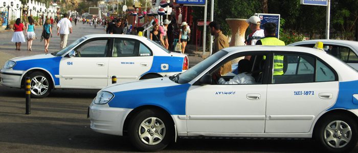 sharm el sheikh taxi white vehicles with blue patches and and a signature yellow roof sign on a busy street