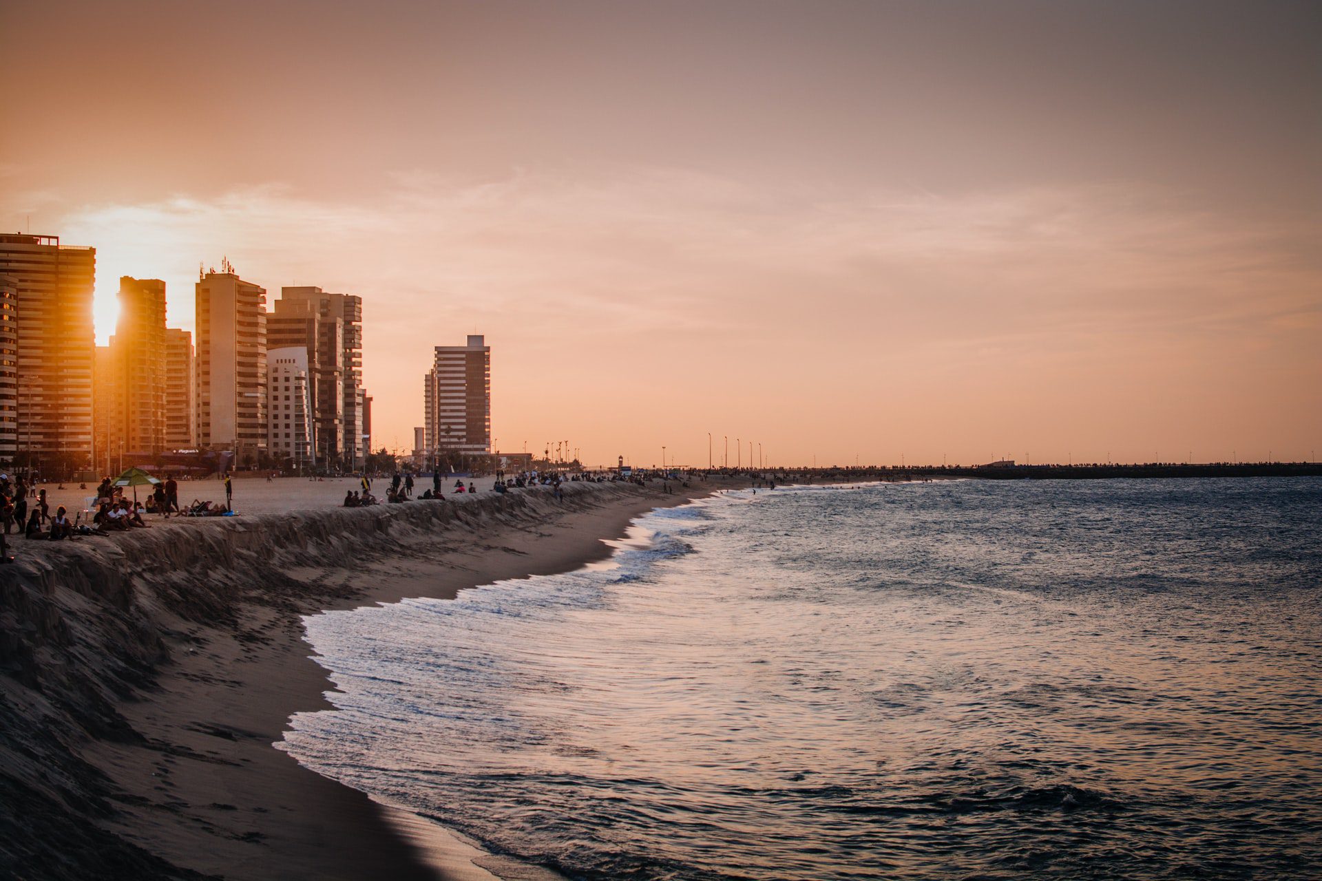 Fortaleza - CE, Brasil sun setting behind high rise city buildings near the sea where people are hanging out