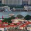 city buildings and houses with red brick roofs by body of water as a boat passes by