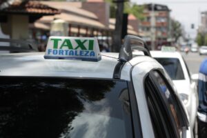 white taxi vehicles on the street with a signature roof sign that states taxi in green and fortaleza in blue capital letters