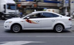 white sedan vehicle with a red and yellow detail on it roaming the street with its signature roof sign