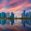 high rise city buildings reflecting onto body of water under a pink and blue sky as the night sets