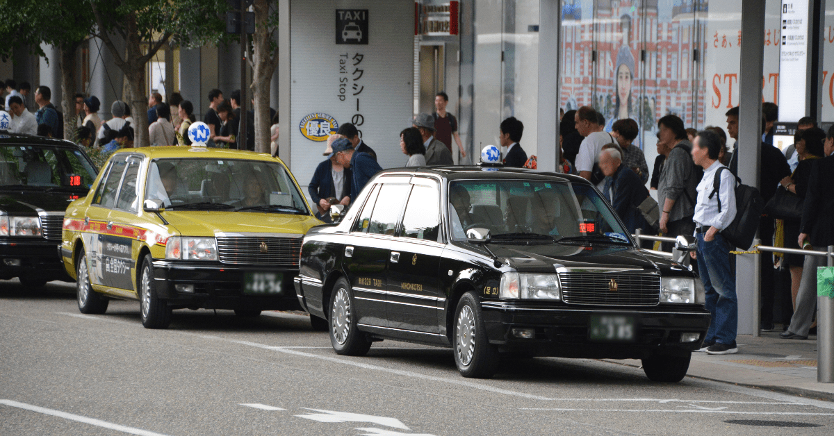 Osaka taxi black taxis and a yellow taxi waiting at a taxi rank by a busy pavement