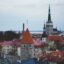 red brick roofs of houses and a tower top in the background under a cloudy daytime sky in Tallinn, Estonia