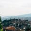 Cityscape shot at daytime, showing mountains at a distance, red brick roof homes and green trees in Sarajevo - Bosnia and Herzegovina - Take a taxi from Sarajevo airport and start exploring