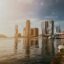 high rise city buildings near body of water and a sky filled with sun rays
