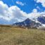 blue sky with big white clouds above a snowy mountain range and a green field