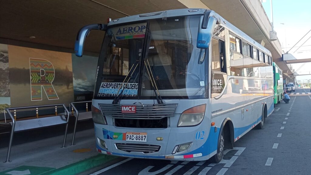 A blue local Quito us parked outside Quito Airport terminal.