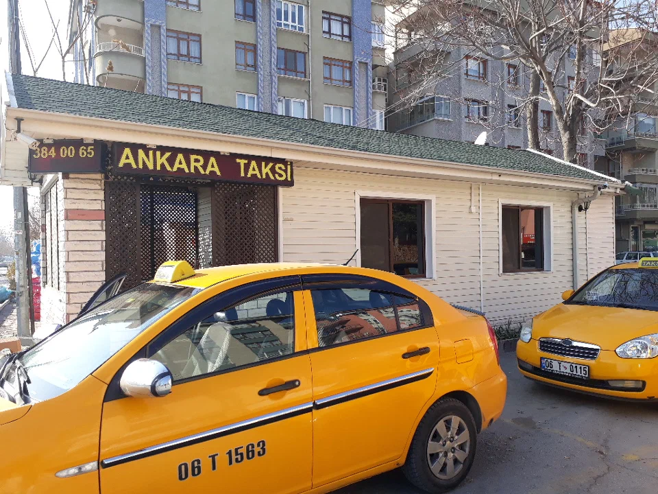 Taxi Ankara A yellow taxi in Ankara, parked outside of a white building with a sign saying 'ANKARA TAXI'.