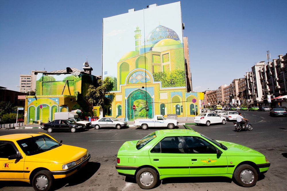 Tehran Taxi Traffic On a Sunny Road and a Mural of a a green mosque on a building's facade