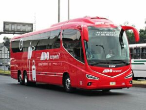 A red ADO bus driving on the road, providing transportation from Cancun Airport, with large windows and luggage compartments visible.