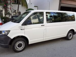 A white passenger minivan parked on a residential street, commonly used as a Cancun Airport taxi for groups or travelers needing extra space for luggage, offering pre-booked airport transportation services.