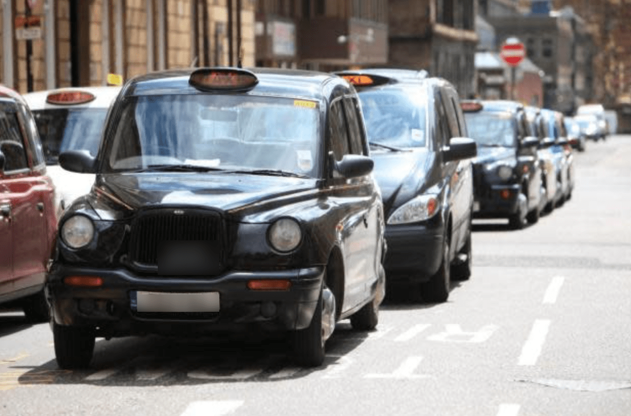Glasgow Taxi A black Hackney Glasgow cab at the front of a taxi rank, with a line of taxis parked behind it and another line to the left.
