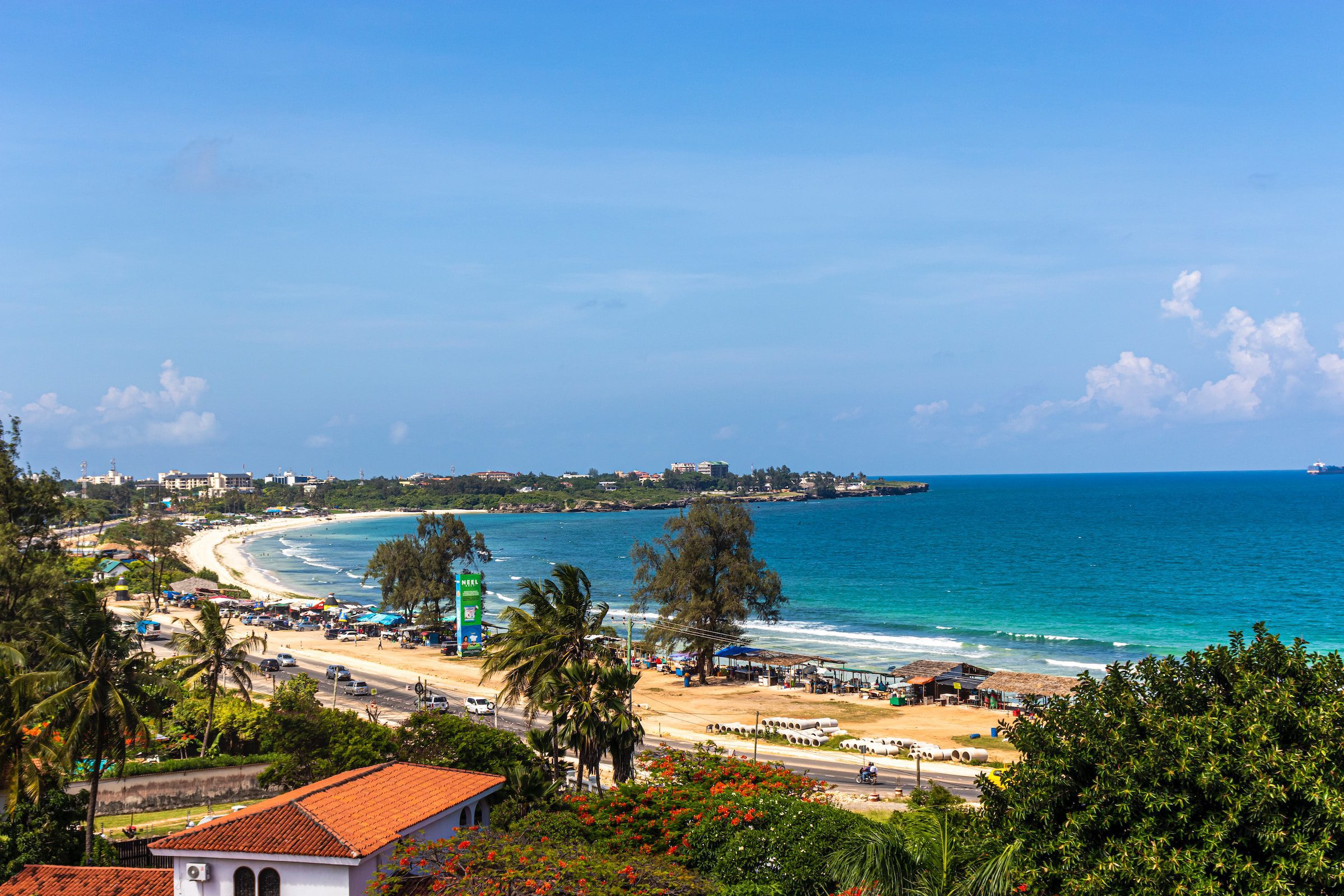 A view of Coco Beach, a road separating the beach from houses and buildings in the background and beach shacks lining the right side of the beach.