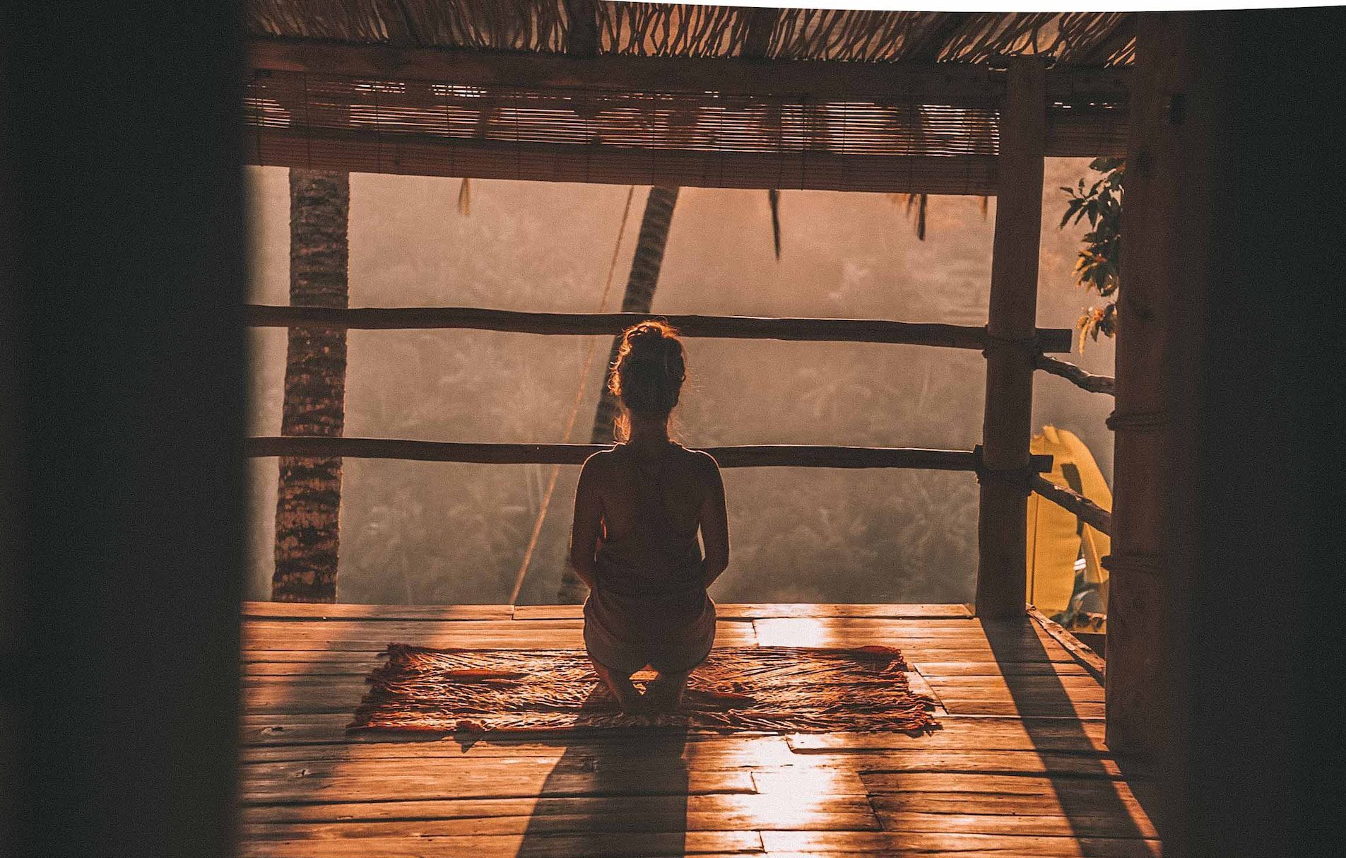 A person sat on the floor meditating in a traditional Balinese hut.