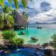 A breathtaking view of Tahiti's natural beauty, with lush forests of the Soar blending into the azure waters of the sea, and a grass hut on the water.
