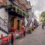 A cobbled street in Glasgow lined with houses either side and with tables and chairs along the left side.