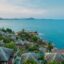 View of the Koh Samui coastline, filled with houses and lush trees, with turquoise waters up ahead.