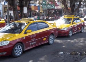Koh Samui Taxi - Welcome Pickups Yellow and burgundy Koh Samui taxis lined up in a rank on the street, with shops behind.