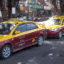 Yellow and burgundy Koh Samui taxis lined up in a rank on the street, with shops behind.