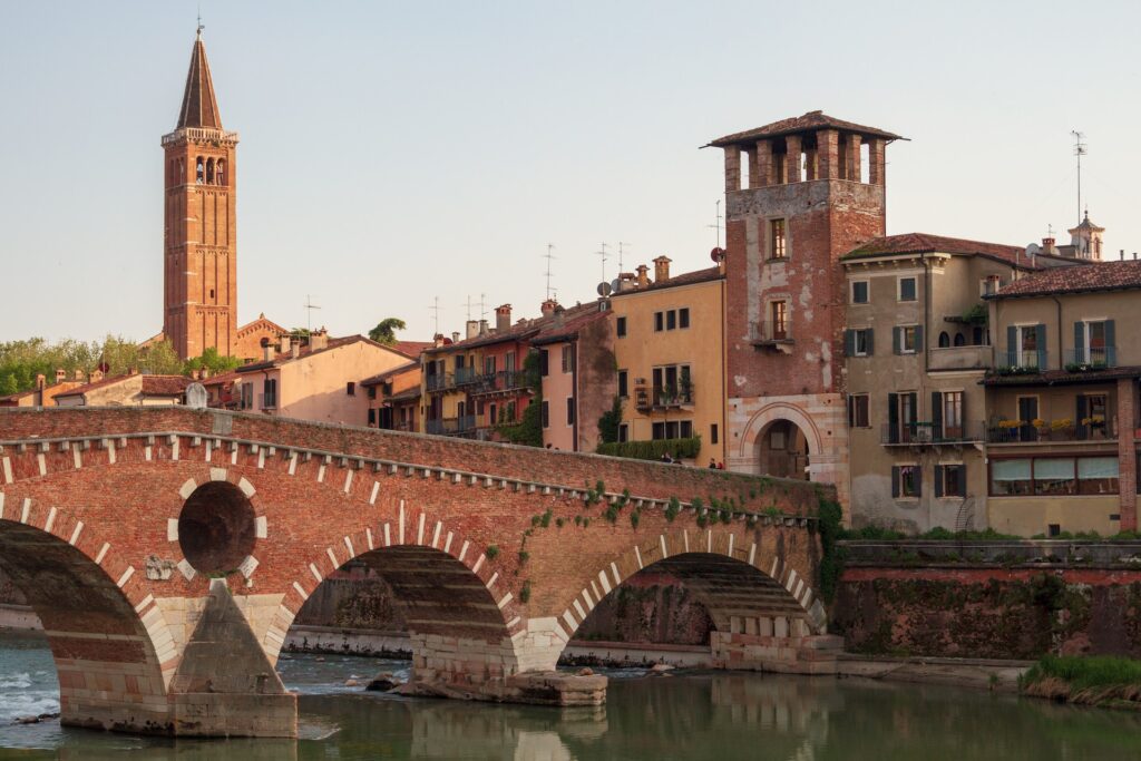 An bridge crossing over into the historic city of Verona filled with brown hues and a church tower in the background.