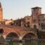 An bridge crossing over into the historic city of Verona filled with brown hues and a church tower in the background.