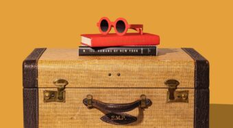 A handheld suitcase with books and a pair of red sunglasses on top, with an orange background.