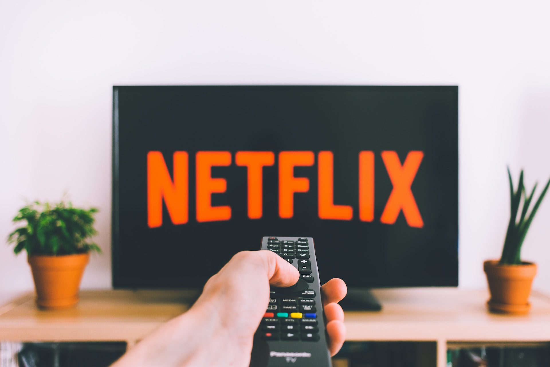 A hand pointing the remote at a TV with the words 'Netflix' on the screen.