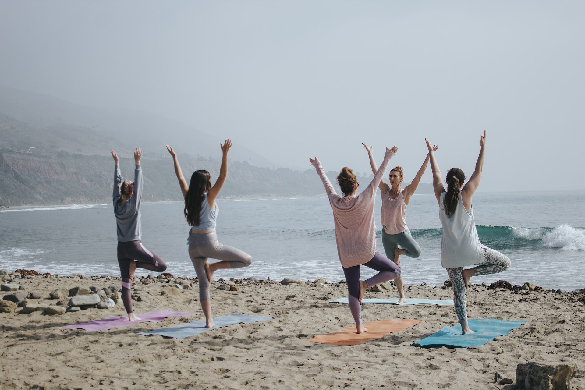 A group of women doing yoga on the beach on a cloudy day.