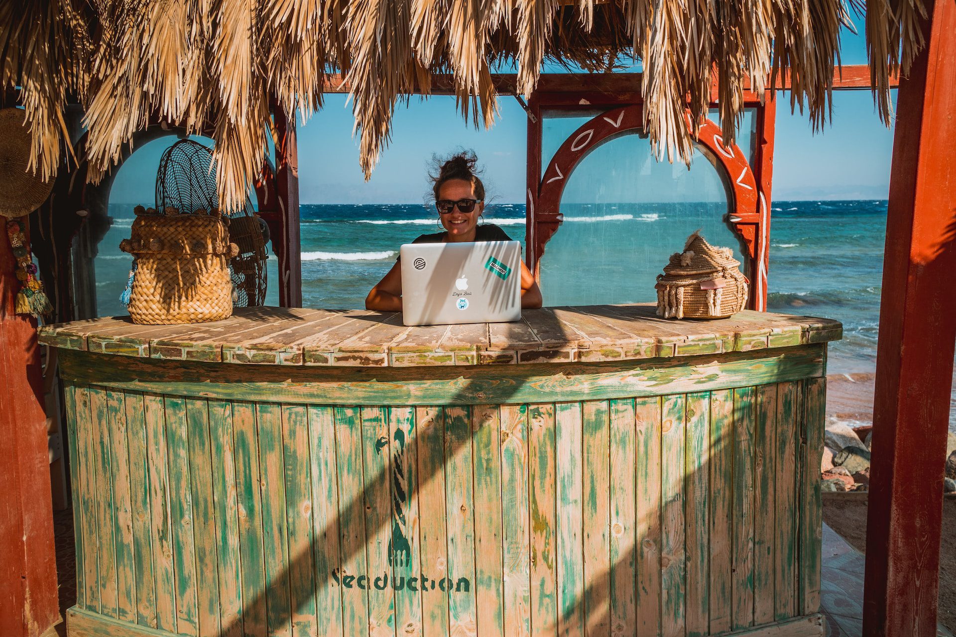 Woman standing at a beach bar, working from her laptop.