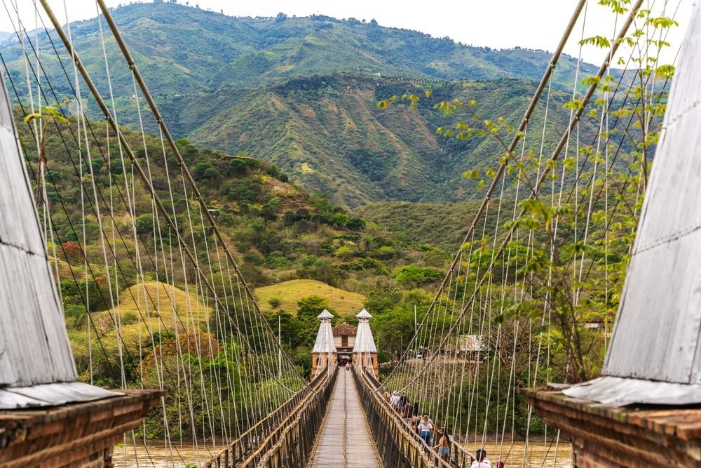 A view from the entrance of the Puente de Occidente suspension bridge with mountains in the background.
